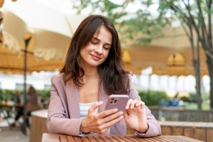 Mulher sentada em ambiente externo olha para o celular