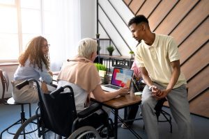 Três pessoas sentadas, sendo uma delas cadeirante, conversam em volta da mesa de trabalho