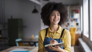 Moça sorridente em pé com mesa de refeitório ao fundo