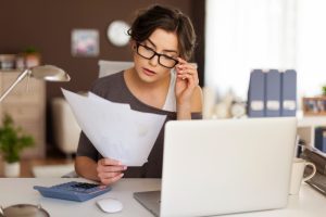 Mulher sentada à mesa de trabalho com computador na frente segurando papeis