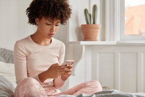 Mulher vê celular sentada na cama