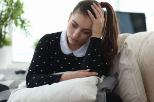 Mulher sentada com expressão desolada coloca uma das mãos na cabeça