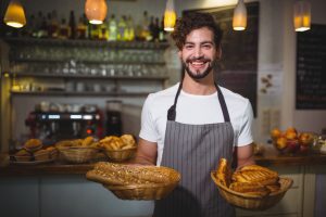 Homem em padaria segura cestas de pães
