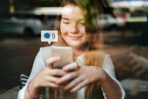 Mulher olha sorridente para o celular com um ícone de caixa de diálogo sobre ele
