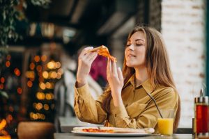  Mulher come fatia de pizza e toma suco de laranja em lanchonete 