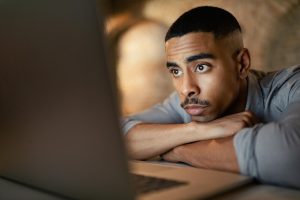 Homem apoia os braços na mesa de trabalho e pratica autossabotagem procrastinando a realização de uma tarefa importante