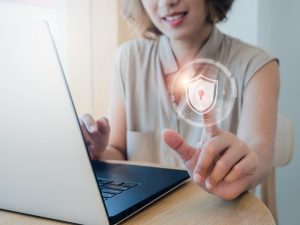 Mulher trabalha em seu notebook e coloca a digital num ícone digital de segurança, representando acesso à conectividade social