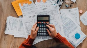 Mulher usa calculadora e coloca diversas notas fiscais sobre a mesa, que usa para realizar as rotinas contábeis de sua empresa