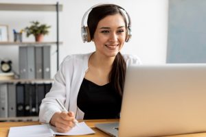 Mulher sorridente faz anotações em treinamento online no laptop
