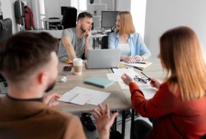 Mesa de reuniões profissional com quatro colaboradores sentados conversando, dois em primeiro plano de costas e dois em segundo plano de frente realizando inbound recruiting