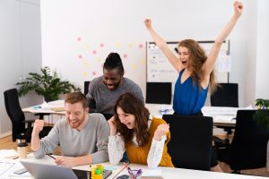 Time profissional com 2 homens e 2 mulheres celebram uma conquista enquanto olham para a tela de um laptop simbolizando orgulho ao entender o que é Employee Value Proposition