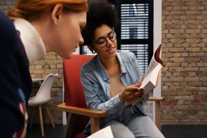 Duas mulheres jovens em ambiente corporativo conversam sobre o que é Employee Value Proposition enquanto uma mostra um livro para a outra