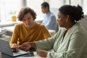 Colegas de trabalho conversando sobre o que é Employee Value Proposition enquanto uma colaborado em primeiro plano mostra algo na tela de um laptop para outro colaborador