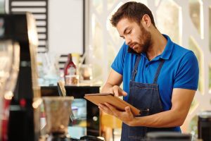 Homem ao telefone em sua lanchonete segura tablet para realizar o registro de sua marca no INPI