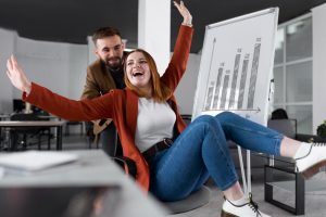 Dois profissionais, um homem e uma mulher, celebram a execução de alta performance no escritório, em frente a um gráfico crescente representado em uma lousa