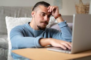 Homem olha com ar de decepção para a tela de seu computador por descobrir que sua marca já foi registrada no Inpi