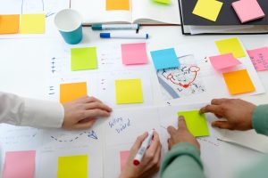 Pessoas trabalham com post-its sobre a mesa simbolizando o uso de métodos ágeis em roadmap