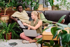 Dois jovens à vontade praticando ócio criativo e conversando e utilizando papéis e um laptop em um ambiente descontraído com plantas