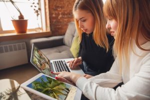 Duas jovens em um ambiente profissional descontraído praticando ócio criativo ao discutir imagens de natureza em um computador e um tablet
