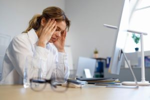 Mulher apoiada sobre a mesa com mãos nas têmporas demonstrando cansaço com desvio de função