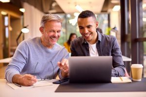 Dois homens sentados à mesa do trabalho estão em processo de coaching para o desenvolvimento de soft skills