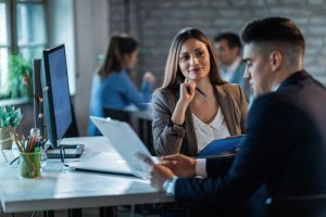 Dois profissionais, um homem e uma mulher estão sentados à mesa em reunião de gestão estratégica 