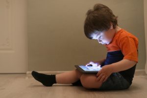 Criança pequena sentada assistindo algo em tablet, expondo-se ao brain rot