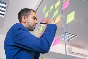 Homem profissional está em pé em um escritório enquanto escreve em post-its colados em um vidro da empresa