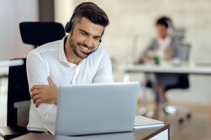colaborador da escala 12x36 em seu escritório, olhando para a tela de seu computador e sorrindo com os braços cruzados 