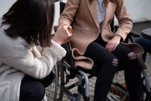 uma mulher segurando a mão de uma pessoa com deficiência de mobilidade, demonstrando o que é capacitismo 
