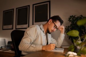 Homem adulto focado, demonstrando resiliência profissional enquanto trabalha até tarde, fazendo anotações em um caderno