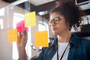 Jovem concentrada organizando post-its em uma superfície de vidro. Elase sente motivada por trabalhar em empresa com alto employer branding
