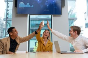 Três profissionais em um ambiente corporativo celebrando com um “high five” a contratação por empresa com employer branding
