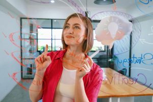 mulher com roupa vermelha desenha em quadro transparente as competências socioemocionais