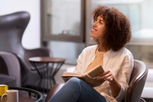 Mulher sentada em uma poltrona confortável, sorrindo levemente demonstrando segurança psicológica no trabalho, enquanto segura um caderno, 
