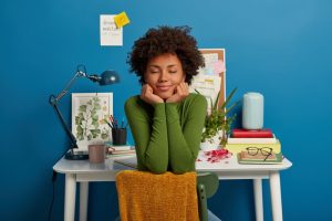 Mulher que vivencia segurança psicológica no trabalho está sentada de costas para uma mesa organizada, com livros, plantas e objetos de escritório ao fundo