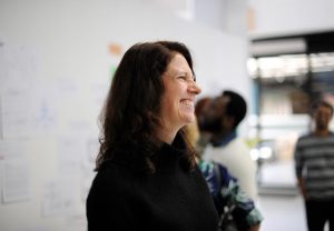 Mulher profissional sorridente, na faixa dos 50 anos, em primeiro plano, em ambiente corporativo
