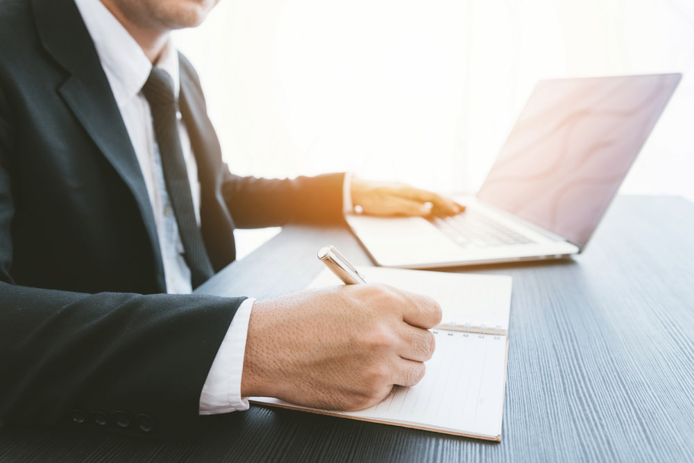 homem de terno usando o computador e consultando caderno