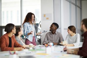 mulher com expressão facial positiva lidera reunião com colaboradores sorridentes sentados à mesa 