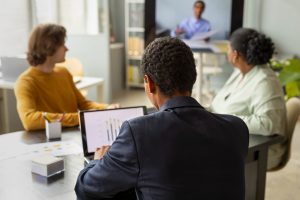 pessoas trabalhando em uma sala de reuniões usando computadores enquanto conversam com outro mais distante