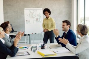 Líder feminina dá treinamento para colaboradores em sala de reuniões e é aplaudida pelos demais