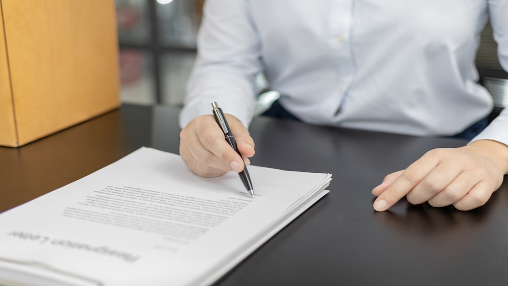 Homem sentado à mesa do escritório escreve sua carta de demissão à mão.
