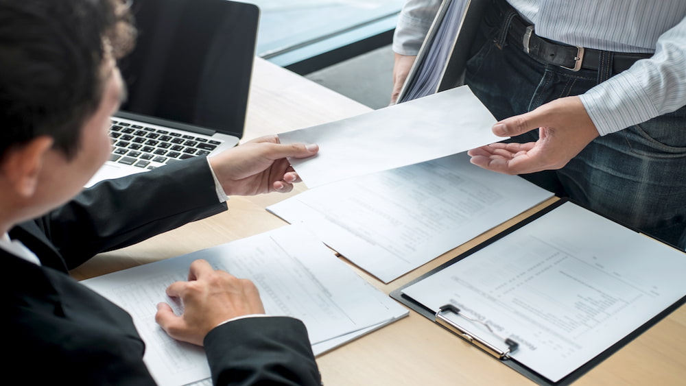 funcionário entrega uma carta de demissão ao seu chefe sentado em sua mesa.